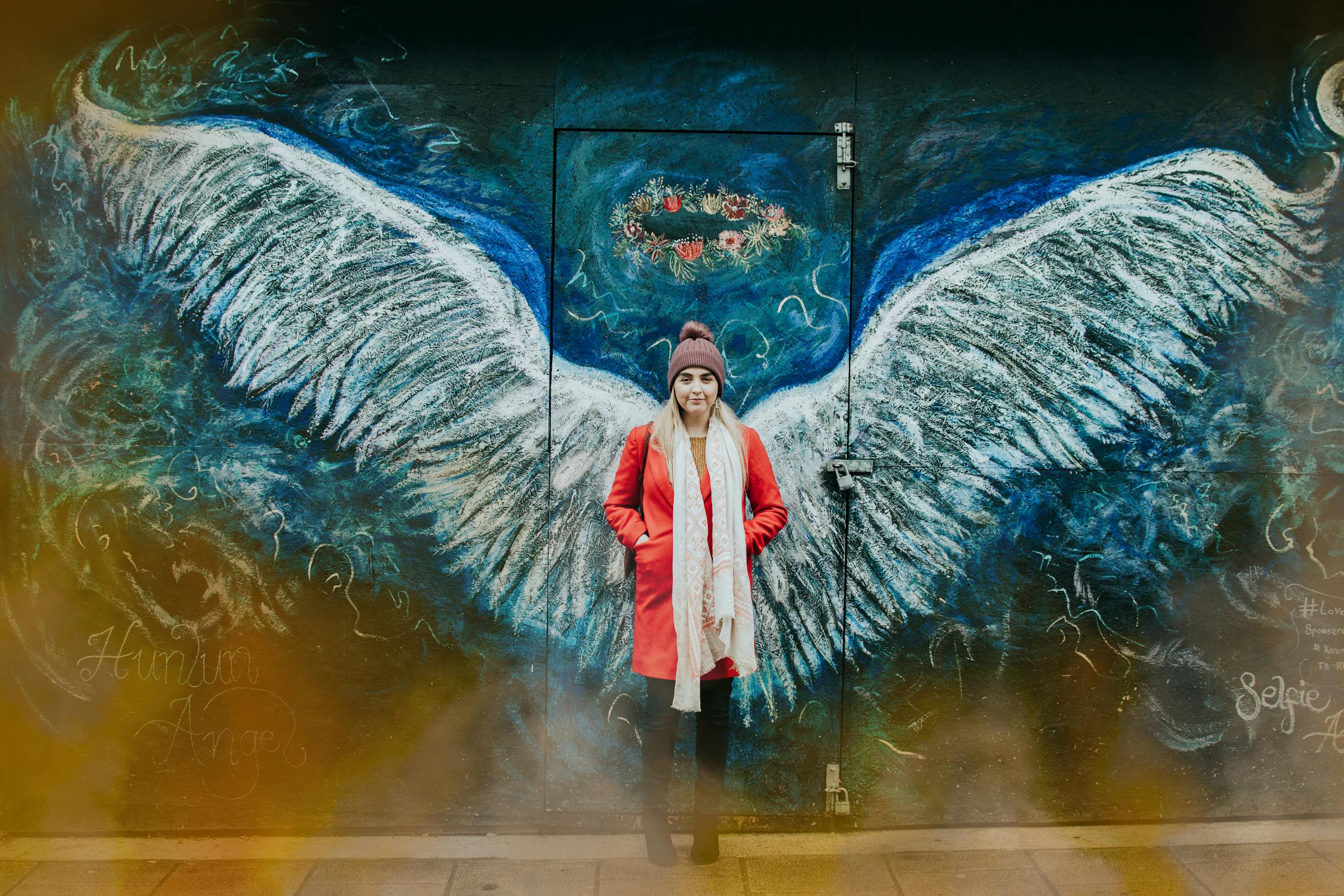 Woman posing in front of angel wings street art in Bangor, Wales.